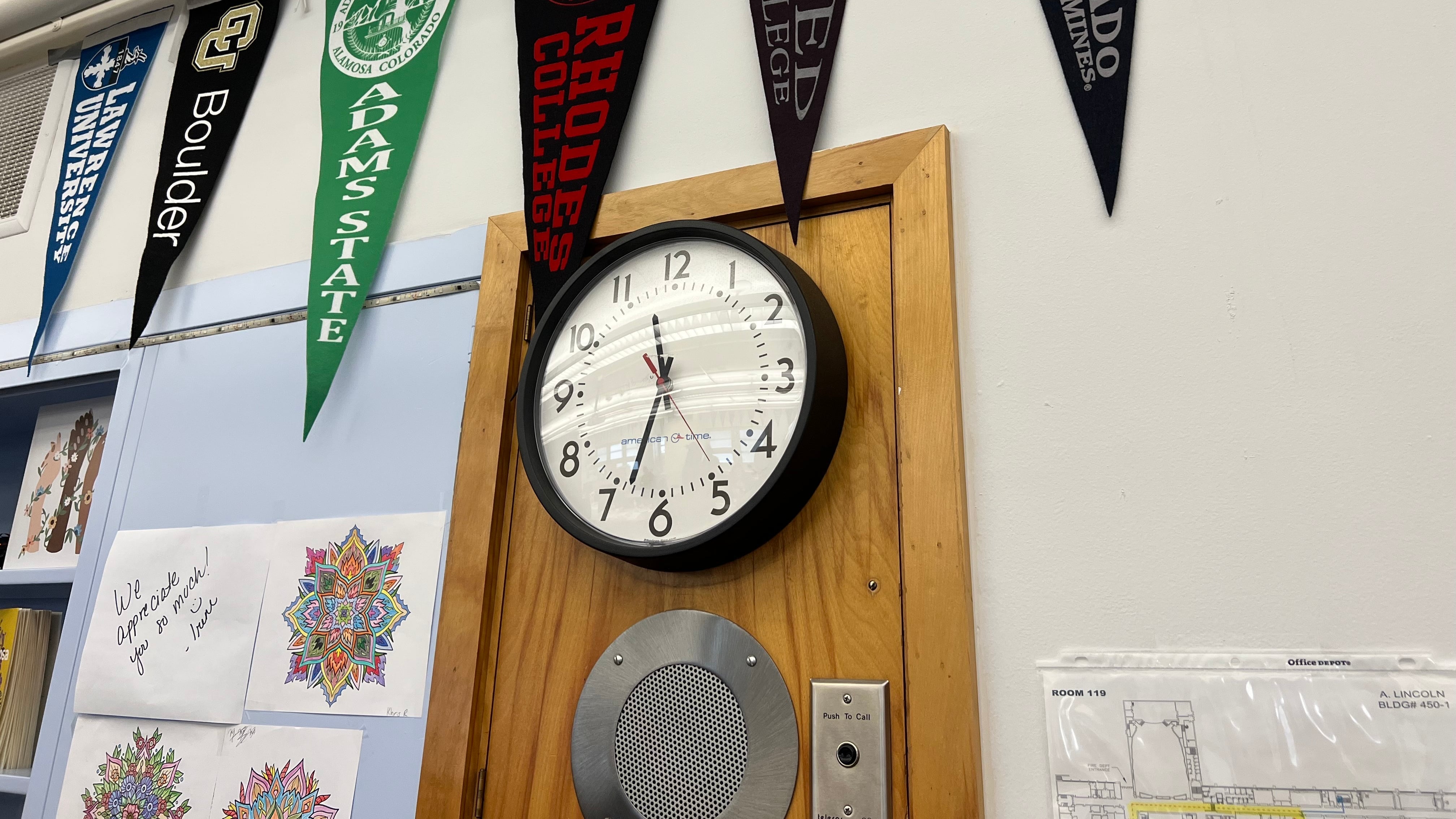 College pennant flags hang inside Lincoln High School in Denver above a clock.
