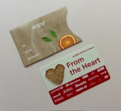 Two pieces of paper on a tan background. One is brown with white words on it and an illustration of an orange and the other is white and red with a photo of a piece of bread in the shape of a heart.